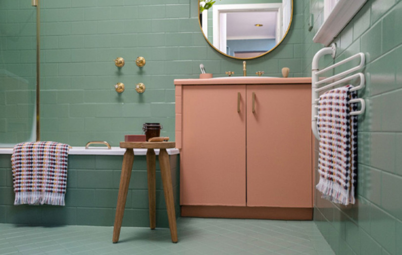 The bathroom tiles are painted in green color, there is a chair and a pink cabinet.
