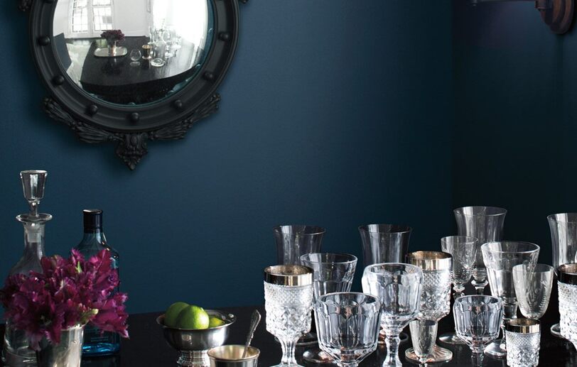 A dark blue-painted dining room wall frames ornate glasses on a table.